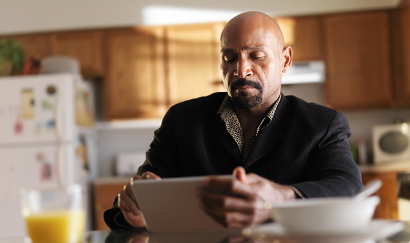 mature african man with tablet in kitchen and breakfast